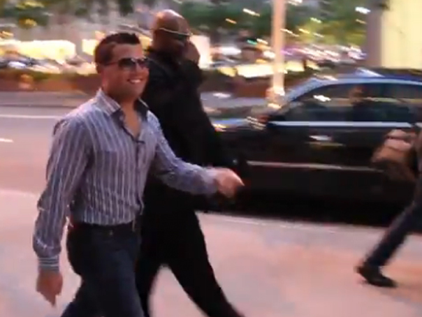 Brett Cohern mergând pe strada acompaniat de bodyguarzi